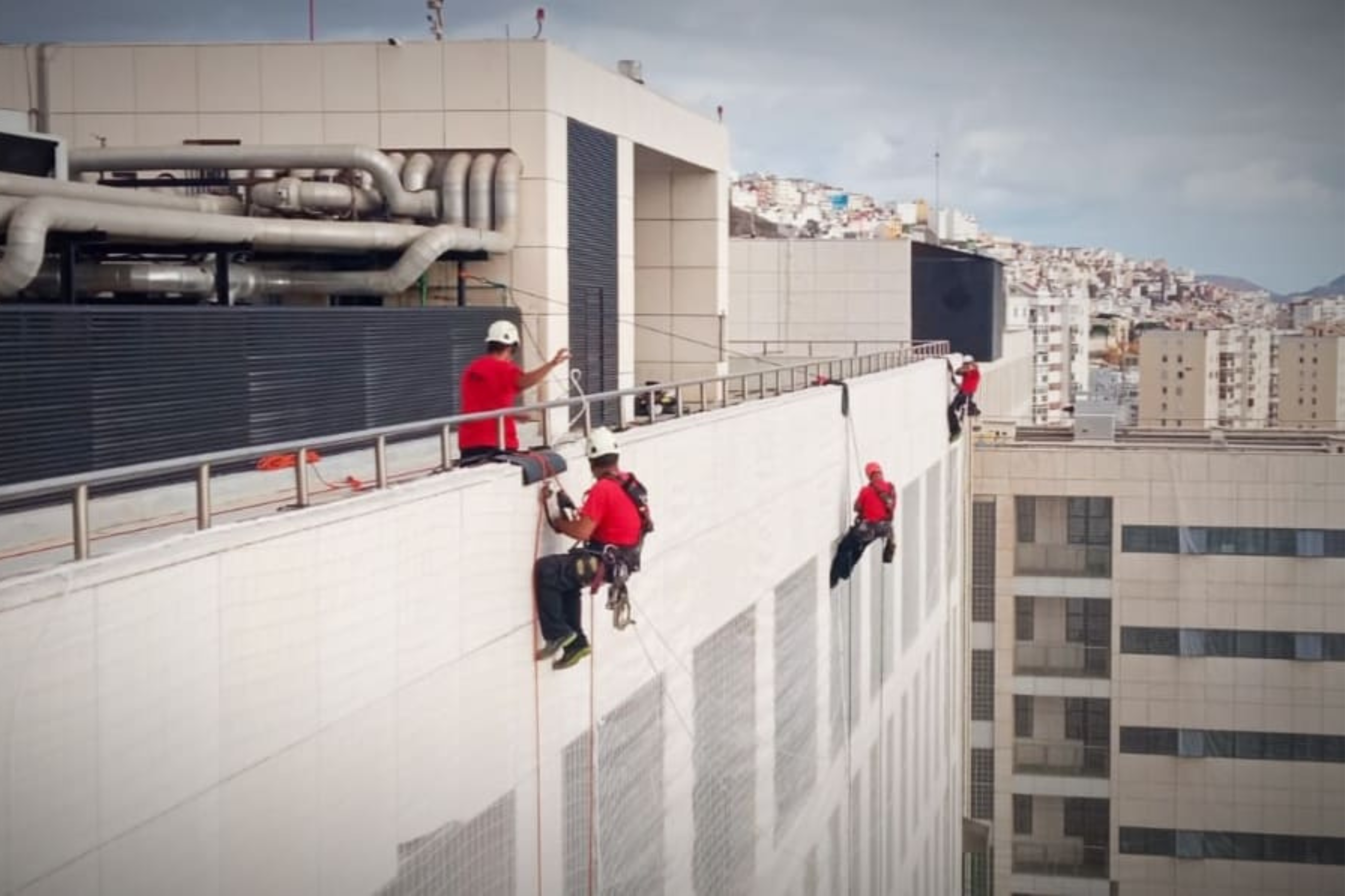 Un grupo de personas realizan tareas mediante trabajos verticales en la fachada de un edificio.