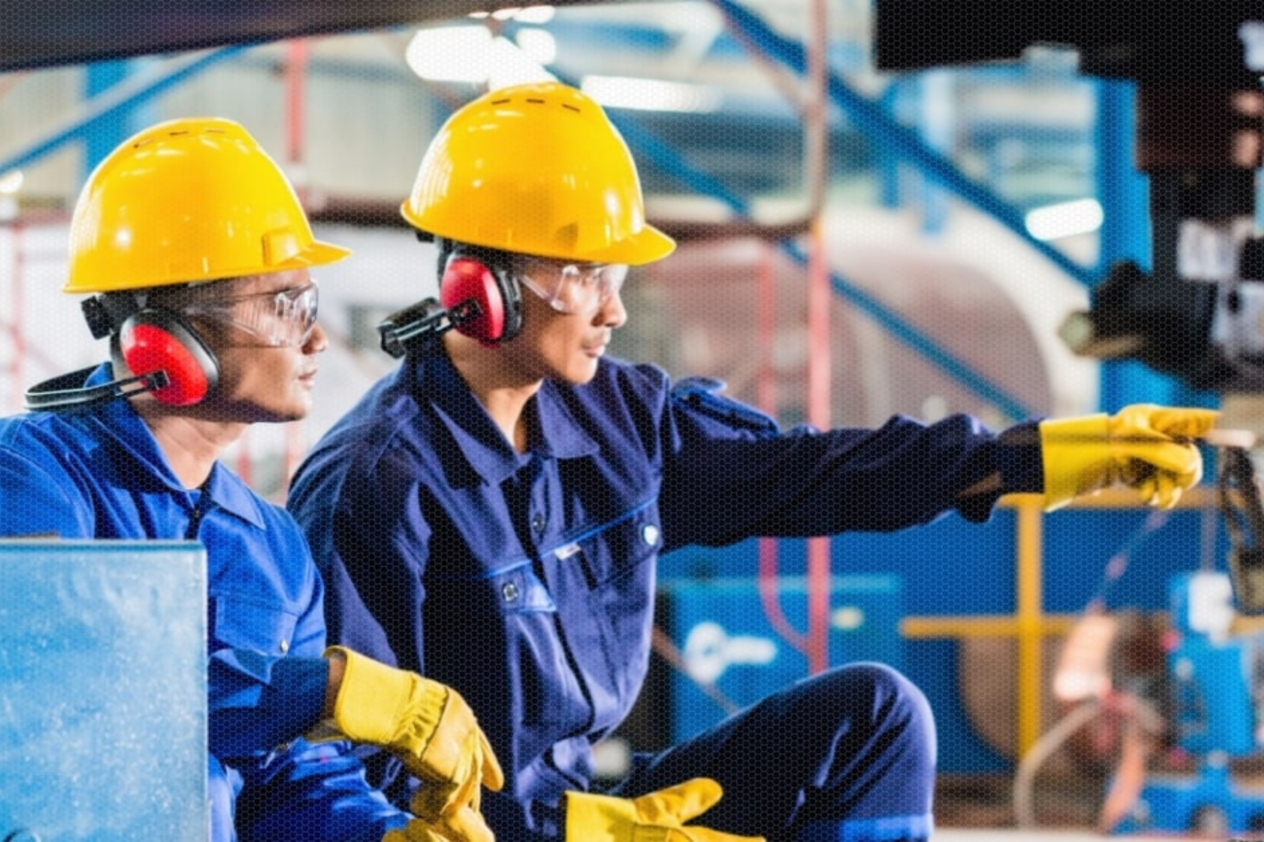 Dos personas vistiendo equipos de protección individual dando indicaciones en una fábrica.