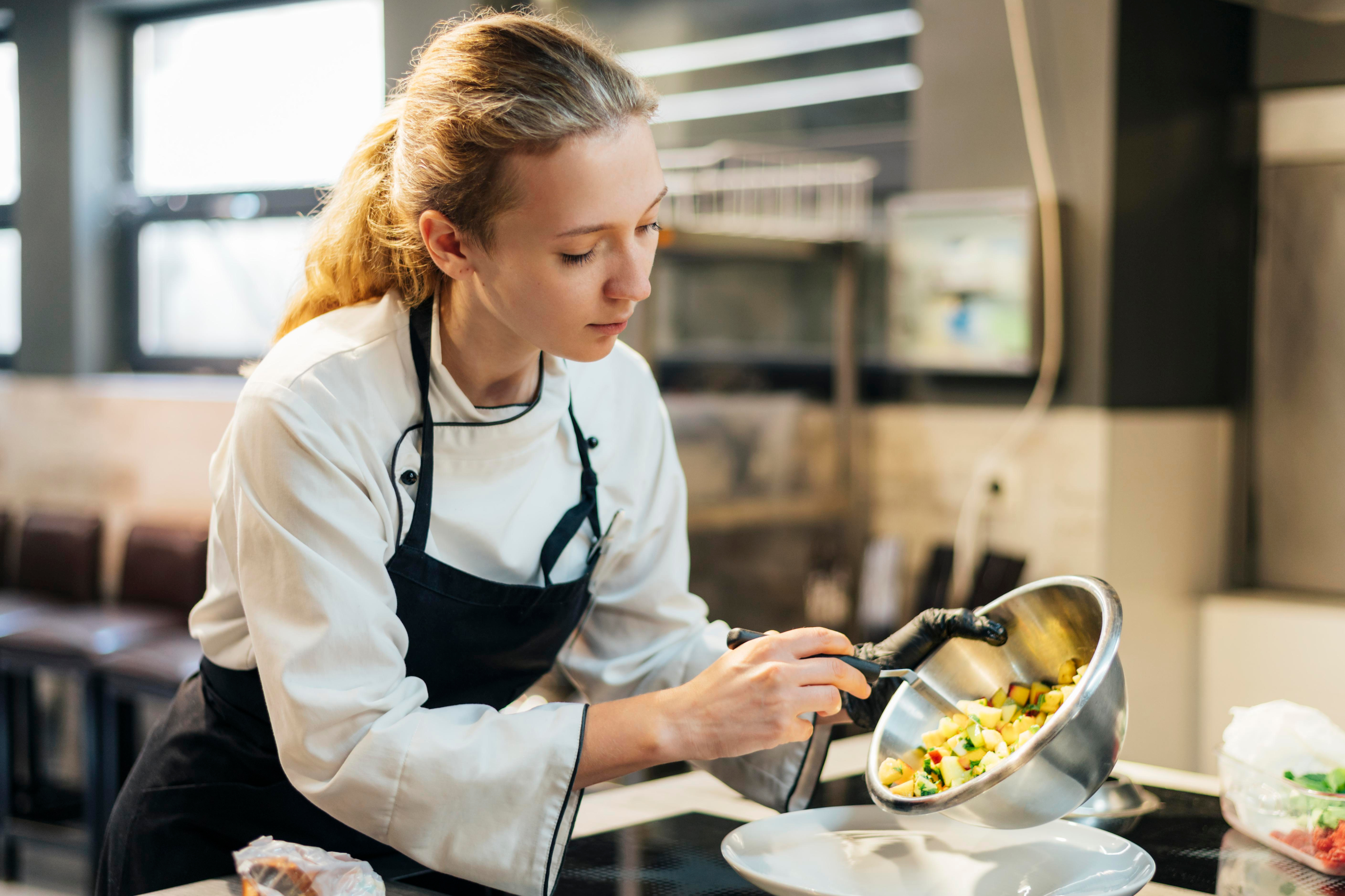 Una jóven cocinera preparando comida en una cocina profesional.