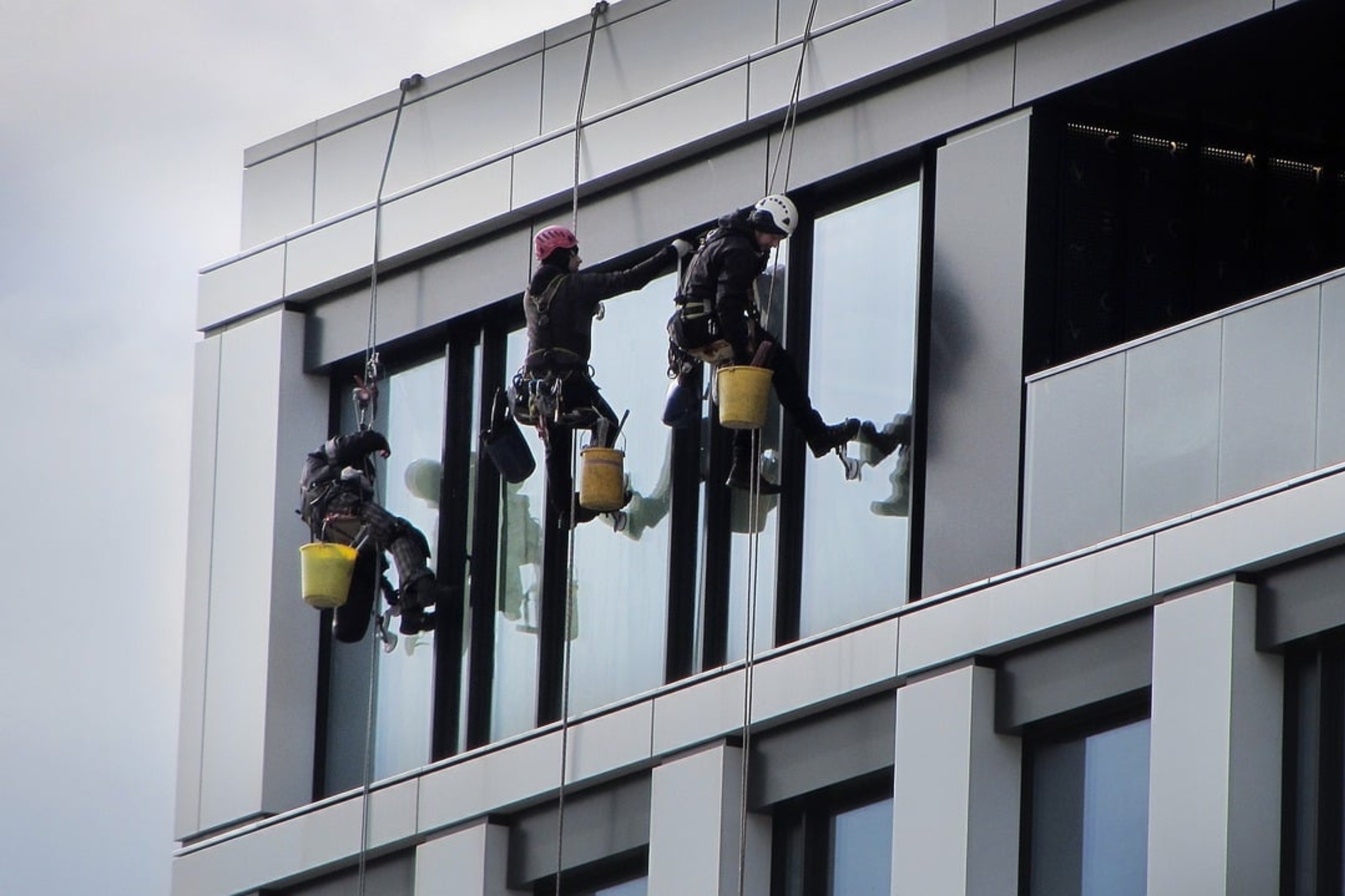Tres trabajadores realizando tareas de limpieza en una fachada mediante trabajos en altura.