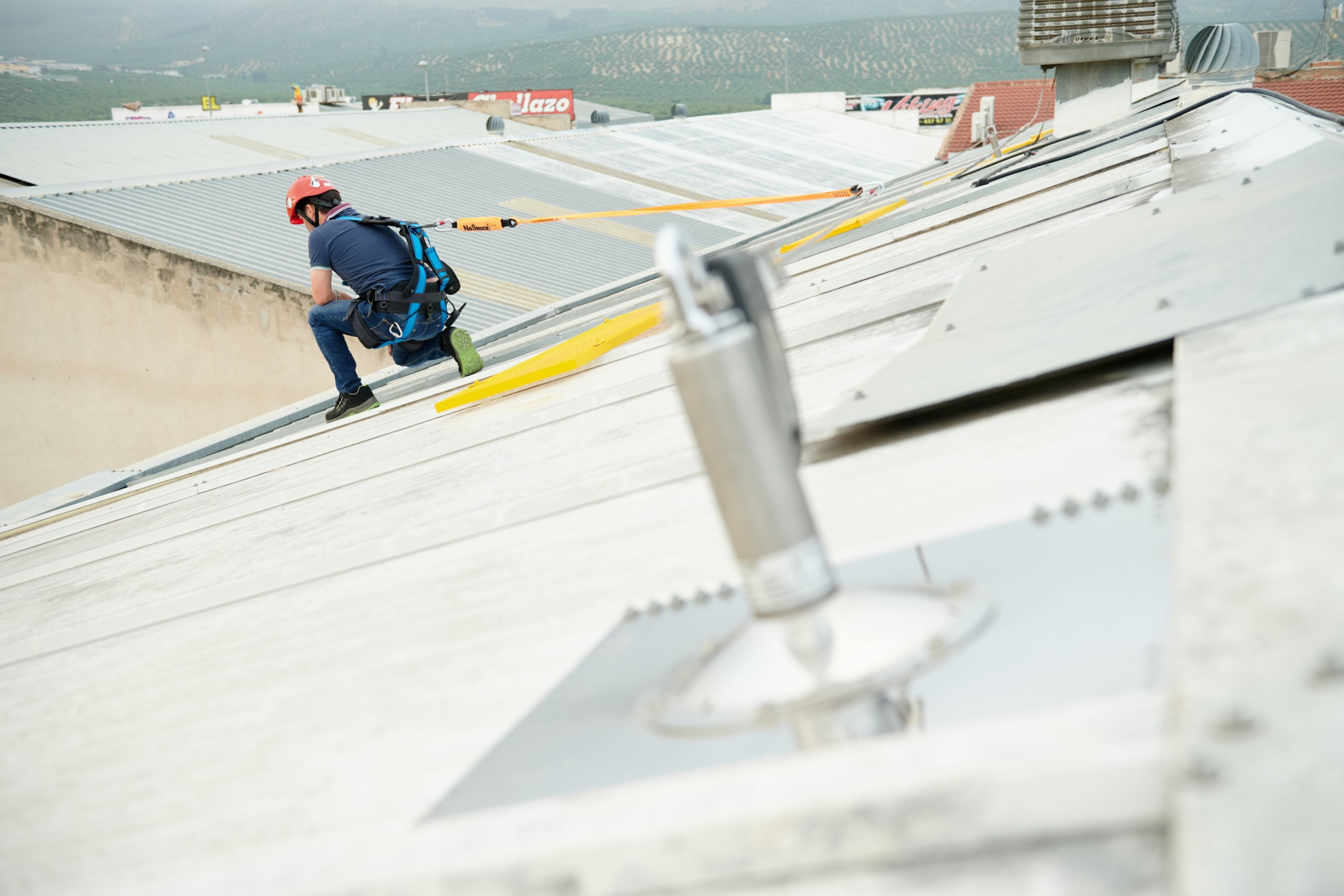 Una persona trabajando en un tejado, anclado a una línea de vida.