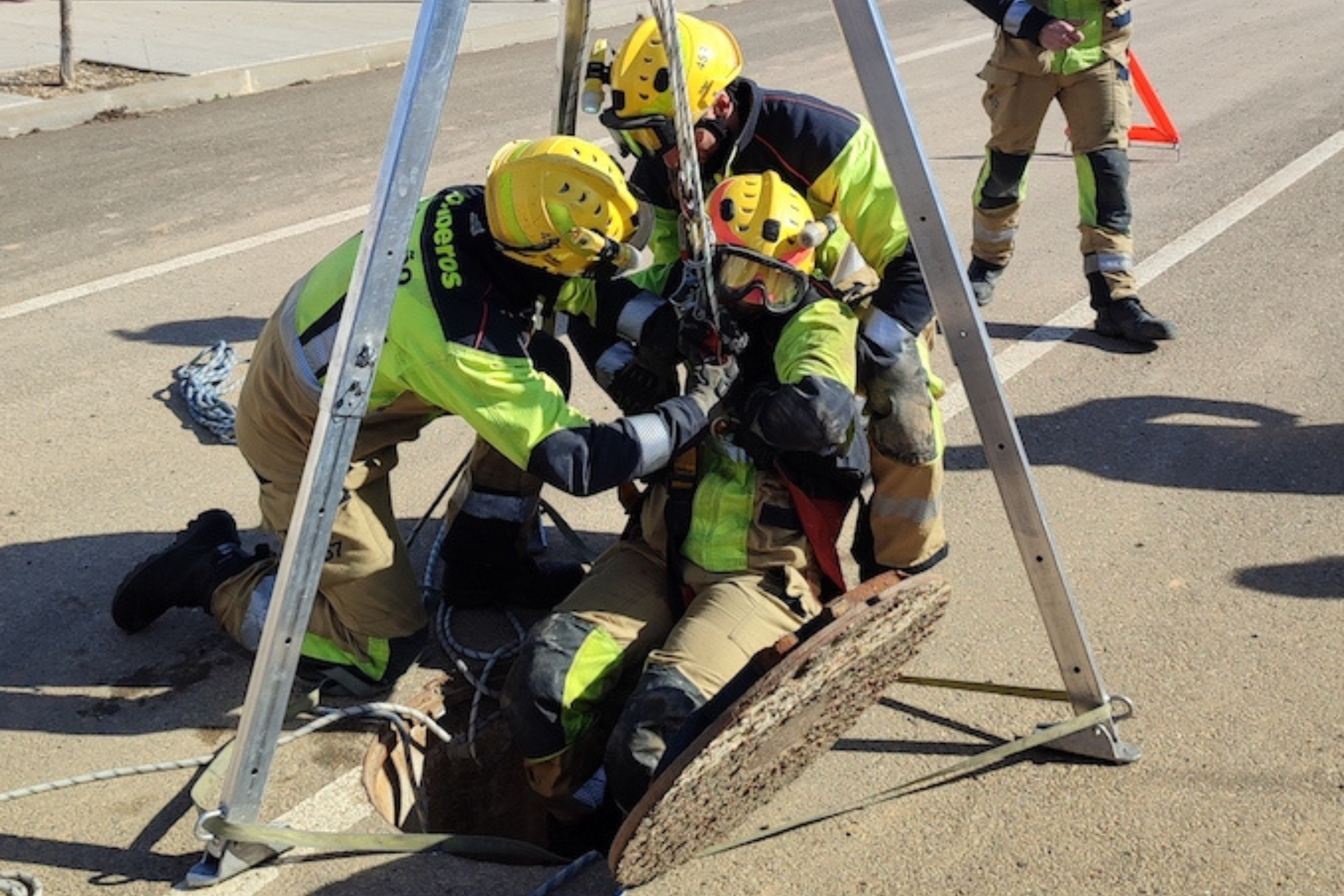 Un grupo de bomberos utilizando un trípode para sacar a otro de un espacio confinado (alcantarilla).