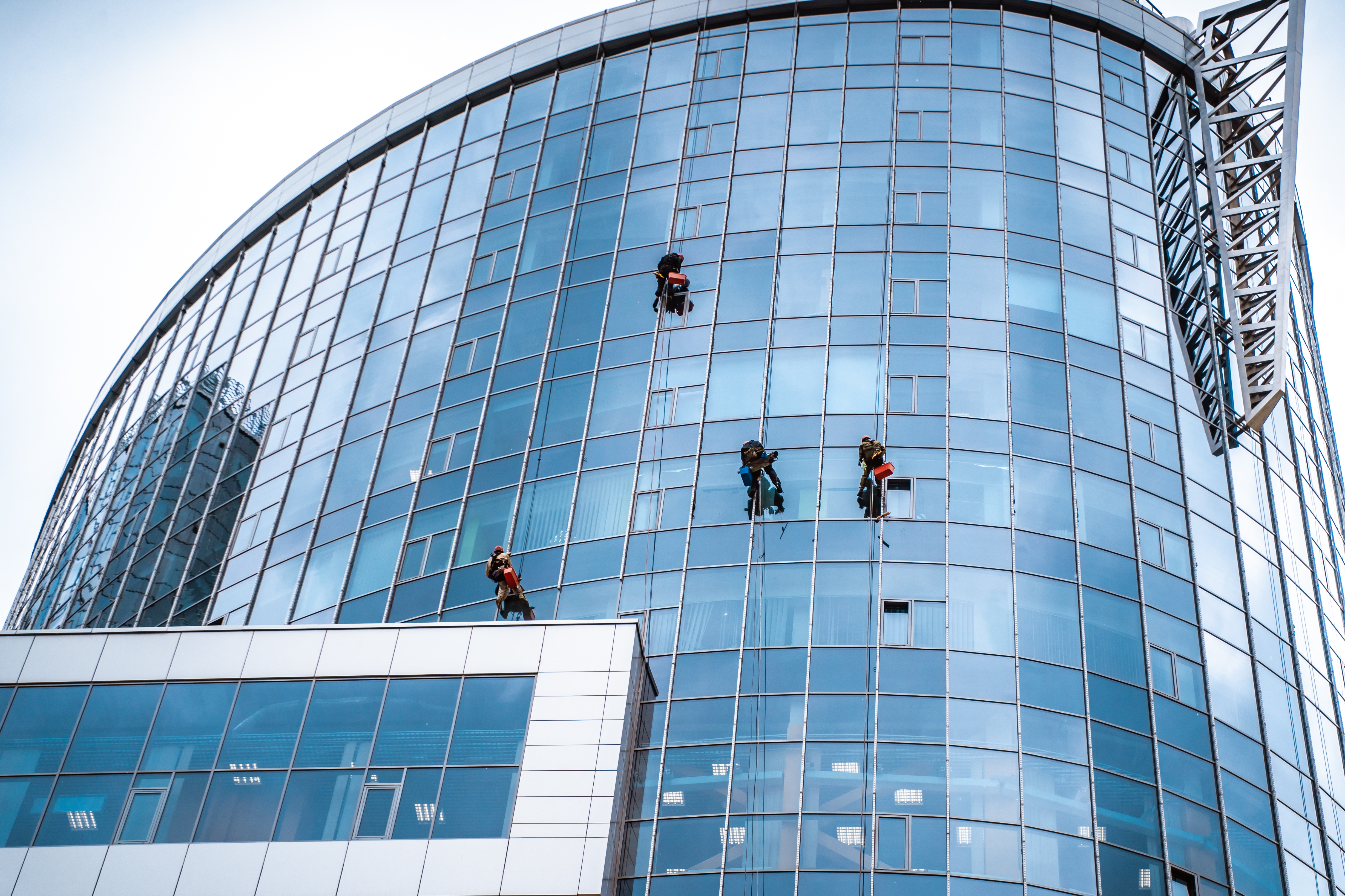Imagen de unos trabajadores realizando tareas en la fachada de cristal de un edificio mediante técnicas de suspensión en trabajos verticales.