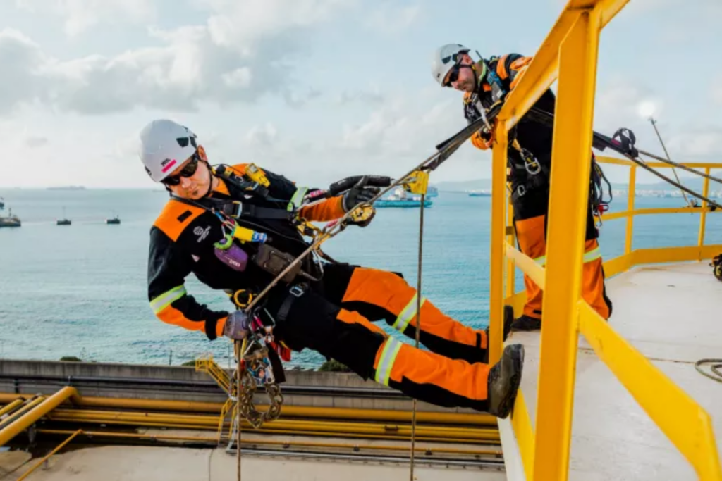 Un trabajador realiza labores de trabajos en altura, mientras que otro supervisa desde arriba