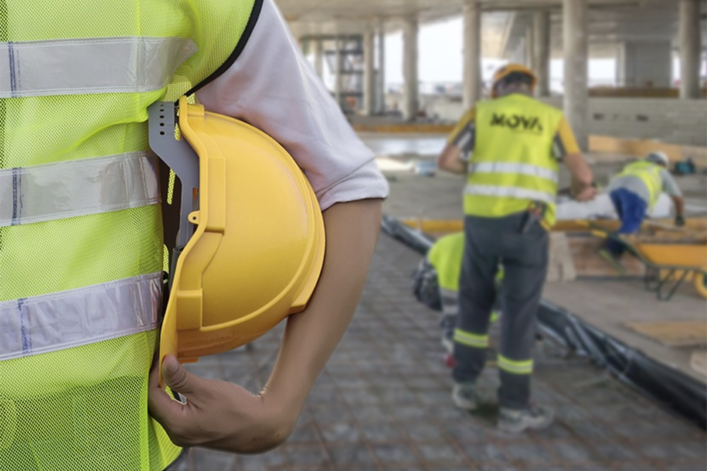 En primer plano aparece una persona (responsable de prevención) vistiendo EPIs, y en segundo plano, aparecen varias personas realizando tareas, mientras visten equipos de protección individual.