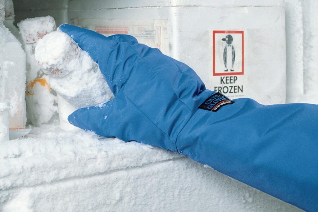 Imagen de la mano de una persona, equipada con guantes térmicos para el frío, realizando su trabajo en un congelador.
