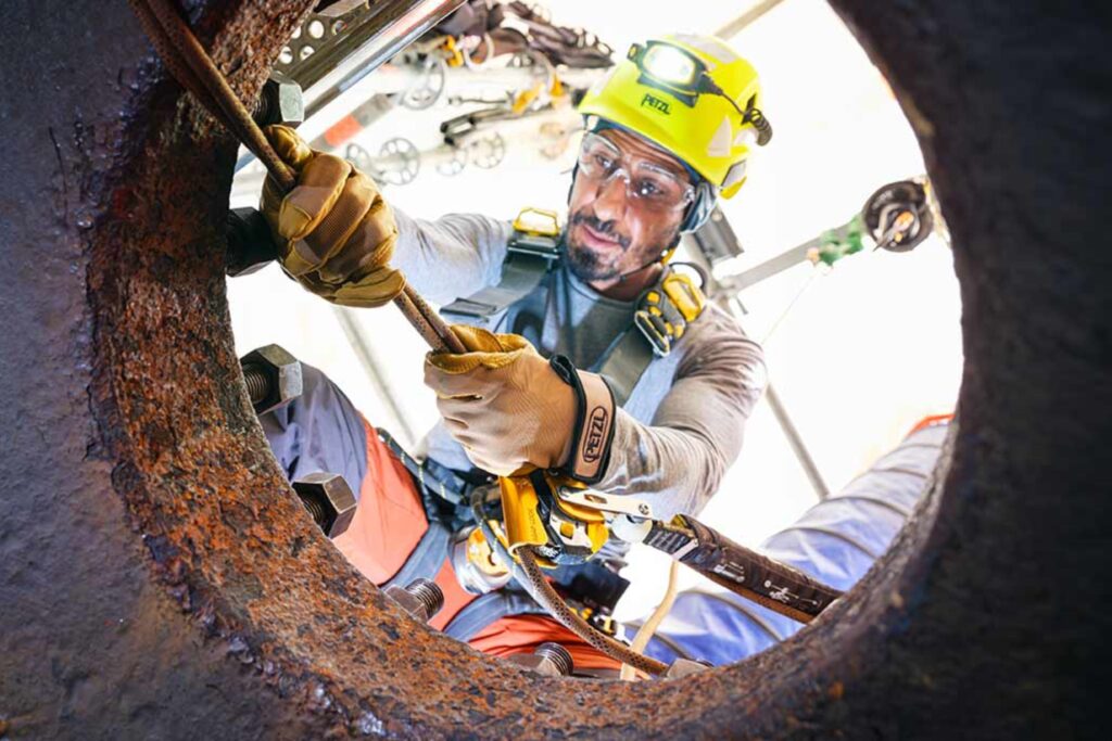 Imagen de un trabajador entrando a un espacio confinado, utilizando iluminación profesional. En este caso una linterna frontal de casco.