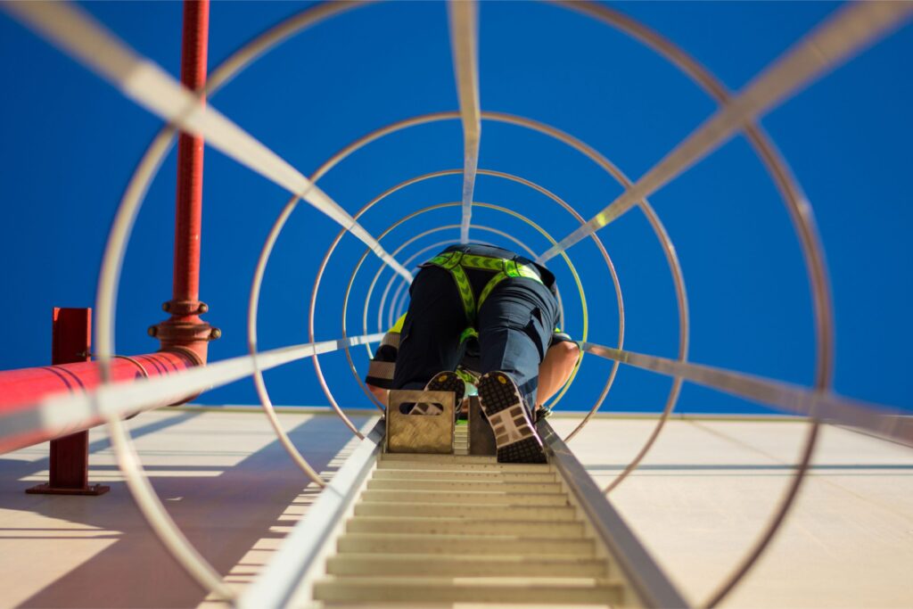 Imagen de un trabajador subiendo una escalera vertical, equipado con los EPIs y sistemas anticaídas correspondientes.